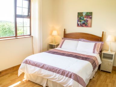 A bedroom with a wooden bed and white bedding beside two nightstands with lamps and a window at Flynns Cottage in Quilty County Clare