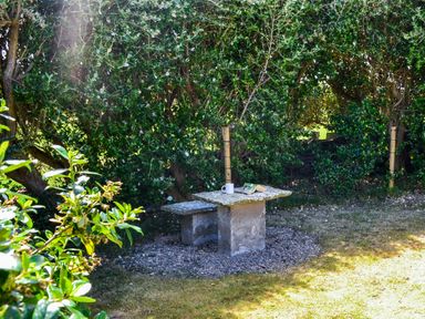 A small stone table with a bench beside it in a garden with green bushes at Flynn's Cottage in Quilty County Clare