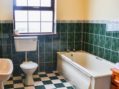A bathroom with a toilet sink bathtub and a tiled floor at Flynns Cottage in Quilty County Clare
