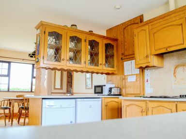 A kitchen with wooden cabinets a microwave a toaster and a dining table with chairs at Flynn's Cottage in Quilty County Clare