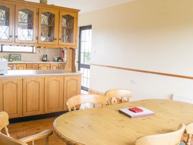 A dining area with a wooden table and chairs next to a kitchen with wooden cabinets and a black door at Flynn's Cottage in Quilty County Clare