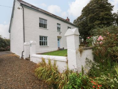 A white two-story house with blue windows and a blue door surrounded by a white wall and garden at Ty Llwyd Nevern near Cardigan