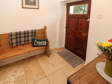 An entryway with a wooden bench holding a plaid blanket and a Croeso pillow a wooden door a striped doormat and a wooden table with a vase of flowers at Ty Llwyd in Nevern near Cardigan