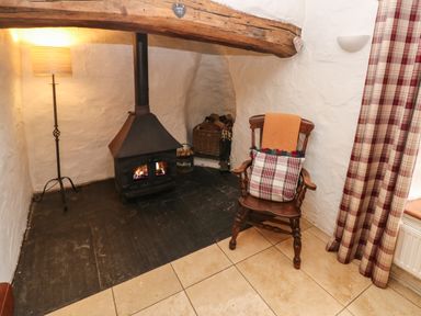 A corner of a room with a wood-burning stove a wooden chair with cushions a floor lamp and a plaid curtain at Ty Llwyd in Nevern near Cardigan