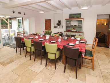 A dining room with a long table covered by a red polka dot tablecloth surrounded by chairs and set with plates cups and flowers at Ty Llwyd in Nevern near Cardigan