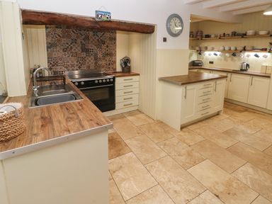 A kitchen with wooden countertops a tiled floor a stove a sink open shelves with dishes and a clock on the wall at Ty Llwyd in Nevern near Cardigan