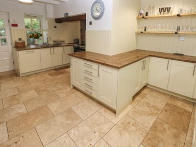 A kitchen with cream cabinets wooden countertops tiled floor and shelves with glassware at Ty Llwyd in Nevern near Cardigan
