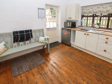 A kitchen with wooden floor a bench with pillows and a blanket and a sink with microwave at Ty Llwyd in Nevern near Cardigan