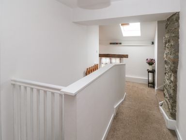 A hallway with carpeted floor a stone wall a small table with flowers and a skylight at Ty Llwyd in Nevern near Cardigan