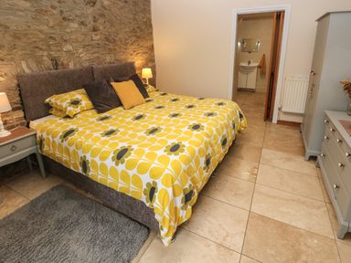 A bedroom with a double bed with yellow floral bedding bedside tables with lamps a wardrobe and a chest of drawers at Ty Llwyd in Nevern near Cardigan