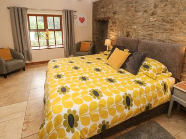 A bedroom with a large bed with yellow floral bedding two armchairs and a window at Ty Llwyd in Nevern near Cardigan