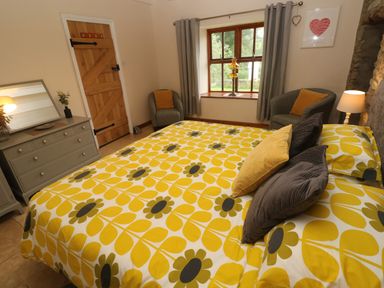 A bedroom with a bed with yellow floral bedding two armchairs a wooden door and a dresser with a mirror at Ty Llwyd Nevern near Cardigan