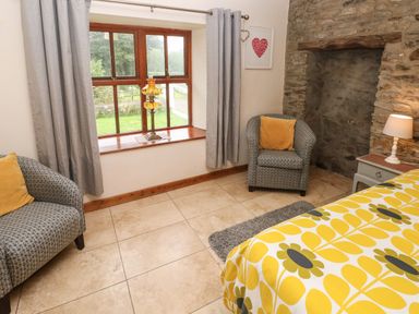 A bedroom with two armchairs yellow patterned bedding and a stone fireplace at Ty Llwyd in Nevern near Cardigan