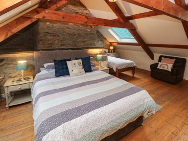 A bedroom with a double bed a single bed a brown armchair wooden beams and a skylight at Ty Llwyd Nevern near Cardigan