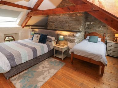 A bedroom with two beds wooden beams exposed stone walls and wooden floor at Ty Llwyd in Nevern near Cardigan