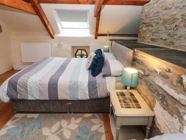 A bedroom with a bed beside a stone wall and a bedside table with a lamp at Ty Llwyd in Nevern near Cardigan