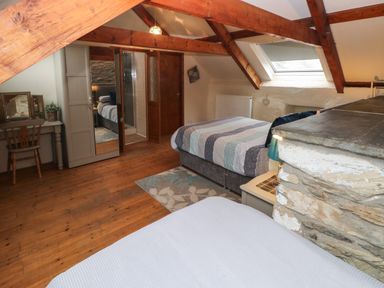 An attic bedroom with exposed wooden beams beds a dressing table and a skylight window at Ty Llwyd Nevern near Cardigan