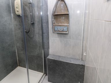 A shower with glass doors and a boat-shaped wall shelf in a tiled bathroom at Ty Llwyd in Nevern near Cardigan