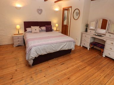 A bedroom with a bed center with bedside tables and lamps and a dressing table with mirror and stool at Ty Llwyd in Nevern near Cardigan