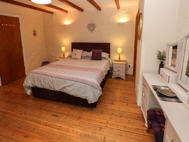 A bedroom with a double bed two bedside tables with lamps a wooden floor and a dressing table at Ty Llwyd in Nevern near Cardigan