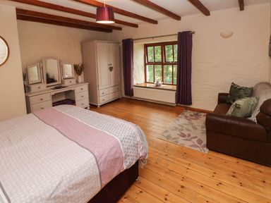 A bedroom with a bed a dressing table wardrobe a window with curtains and a couch at Ty Llwyd in Nevern near Cardigan