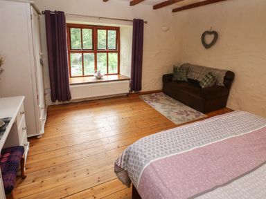 A bedroom with a bed a brown sofa a window with purple curtains and wooden floor at Ty Llwyd in Nevern near Cardigan