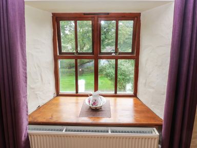 A wooden window sill with a floral pitcher and basin on a mat and purple curtains at Ty Llwyd in Nevern near Cardigan