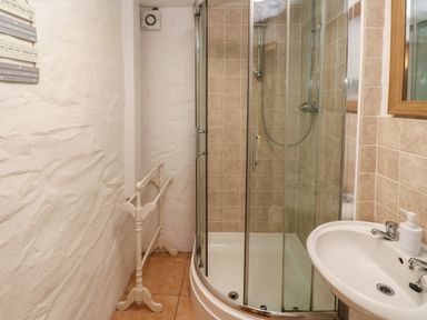 A bathroom with a curved glass shower enclosure a white sink with a soap dispenser and a towel rack on a textured wall at Ty Llwyd in Nevern near Cardigan
