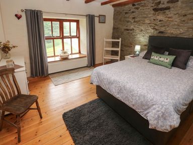 A bedroom with a bed a wooden chair a window with curtains and a stone wall at Ty Llwyd in Nevern near Cardigan