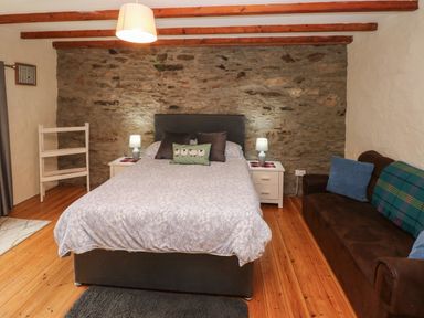 A bedroom with a bed between two bedside tables with lamps and a sofa with cushions near a stone wall at Ty Llwyd in Nevern near Cardigan