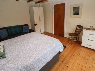 A bedroom with a bed covered in a white and blue floral bedspread a brown sofa with blue cushions a white wardrobe a wooden chair a white dresser and a mirror on the wall at Ty Llwyd in Nevern near Cardigan