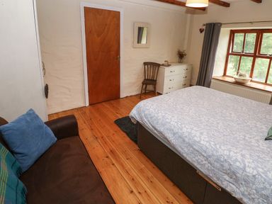 A bedroom with a bed a brown sofa a wooden chair a white dresser and a window at Ty Llwyd in Nevern near Cardigan