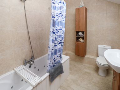 A bathroom with a bathtub with a shower curtain a towel a wooden cabinet with rolled towels a toilet and a sink at Ty Llwyd in Nevern near Cardigan