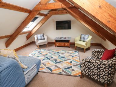 A seating area with four chairs a patterned rug a small table a wall mounted television in an attic room with wooden beams at Ty Llwyd in Nevern near Cardigan