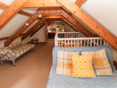 An attic room with wooden beams a blue sofa with yellow pillows a floral patterned bench a small table with chess set and a bedroom at Ty Llwyd Nevern near Cardigan