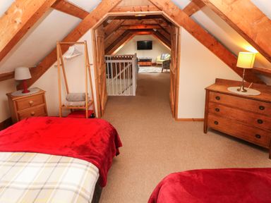 An attic bedroom with wooden beams two beds with red blankets wooden furniture and a sitting area with a TV at Ty Llwyd in Nevern near Cardigan
