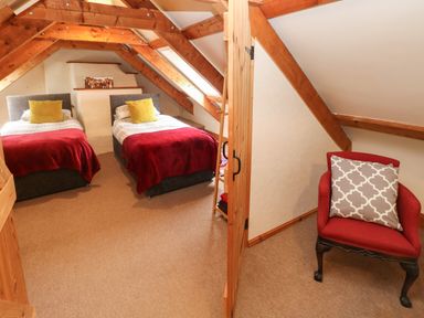 A bedroom with two single beds under wooden beams and a red chair with a patterned cushion at Ty Llwyd in Nevern near Cardigan
