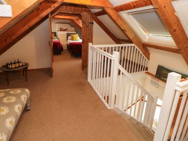 An attic bedroom area with two single beds visible through wooden doors a staircase with white railings and a small table with a chess set at Ty Llwyd in Nevern near Cardigan