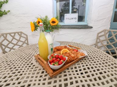 A patio table with a wooden tray holding croissants strawberries a bottle of milk and a bottle of juice with sunflowers in a vase by a window at Ty Llwyd in Nevern near Cardigan