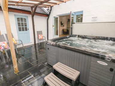 An outdoor patio with a hot tub gray chairs with colorful cushions and blue doors at Ty Llwyd in Nevern near Cardigan