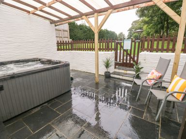 A covered outdoor patio with a hot tub two chairs with cushions and a wooden gate at Ty Llwyd in Nevern near Cardigan