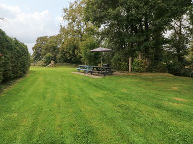 A grassy garden with picnic tables and an umbrella near trees at Ty Llwyd in Nevern near Cardigan