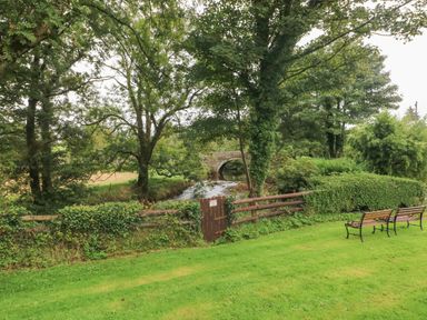 A garden with benches a small wooden gate a stone bridge a stream and trees at Ty Llwyd in Nevern near Cardigan