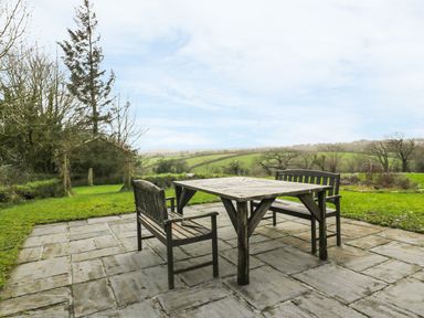 An outdoor patio with a wooden table and benches overlooking a green landscape at Lower West Curry Farmhouse in Launceston