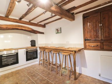 A kitchen with wooden beams on ceiling two ovens a wooden breakfast bar with four stools and wooden cabinets at Lower West Curry Farmhouse in Launceston