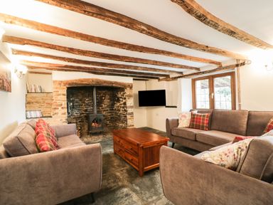 A living room with exposed wooden beams stone fireplace with wood burner sofas and a wooden coffee table at Lower West Curry Farmhouse in Launceston