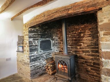 A wood burning stove with firewood in a stone fireplace at Lower West Curry Farmhouse in Launceston