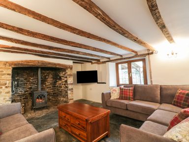 A living room with wooden ceiling beams a stone fireplace wood stove two sofas a wooden coffee table and a wall mounted TV at Lower West Curry Farmhouse Launceston