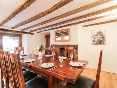 A dining room with a wooden table set with plates and glasses under exposed wooden beams at Lower West Curry Farmhouse in Launceston