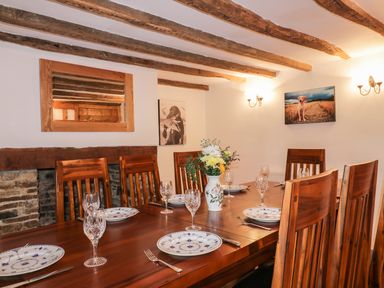A dining room with a wooden table and chairs set with plates glasses and cutlery with flowers in a vase on the table at Lower West Curry Farmhouse in Launceston